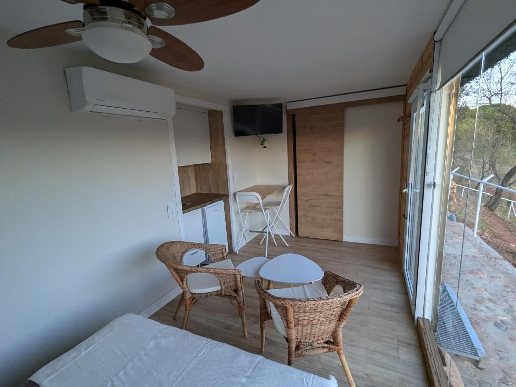 Ein Zimmer mit einem Bett, einem Deckenventilator, einem an der Wand montierten Fernseher, Korbmöbeln und Blick durch eine Glastür.