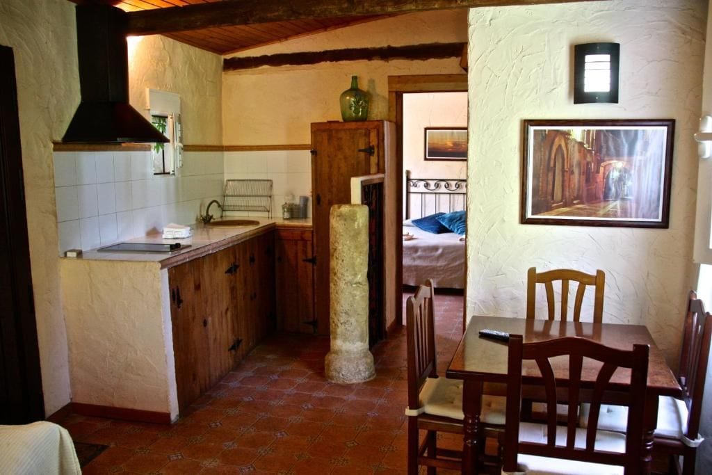 Une cuisine compacte avec un comptoir en bois, un pilier en pierre et un coin repas comprenant une table et des chaises.