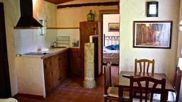Une cuisine compacte avec un comptoir en bois, un pilier en pierre et un coin repas comprenant une table et des chaises.