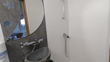 Un bagno con lavabo in pietra, uno specchio, una doccia e un portascopevoli.