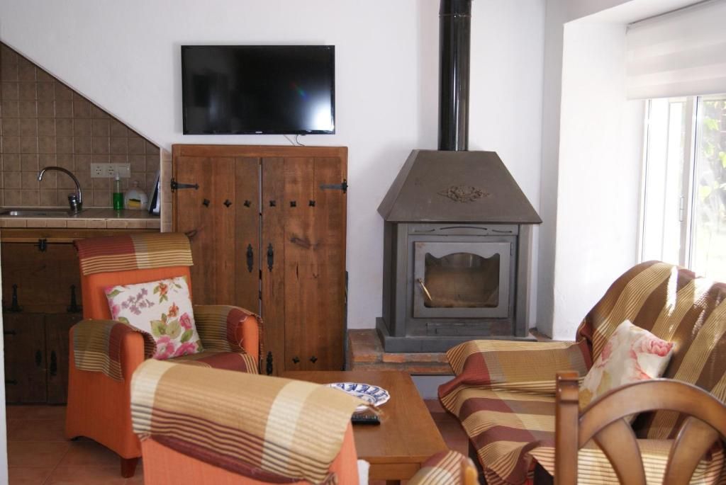 Een woonkamer met een open haard, een aan de muur bevestigde televisie en een keuken met een spoelbak en kasten.