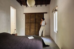 A bedroom with a bed, a wardrobe, a window, and a bedside table with a book and a vase.