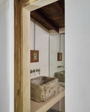 Un baño con un lavamanos de piedra, un marco de madera con un cuadro y un espejo que refleja la habitación.