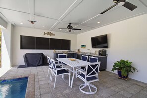 Ein überdachter Außenbereich zum Essen mit Tisch und Stühlen, einem Deckenventilator und einer Fischdekoration an der Wand.