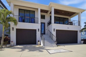 A modern two-story house with a covered staircase, large garage doors, and a balcony. - Manatee Bay Oasis- Waterfront Luxury + Heated Pool (Bradenton)