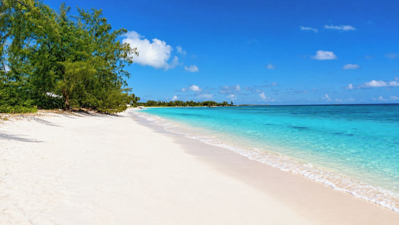A beach with clear turquoise water, white sand, and green foliage.