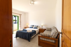 A bedroom with a bed, a sofa, two bedside tables, and a window with curtains. - Vilamoura Garden Villa 2 by Homing (Loulé)