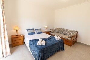 Ein Schlafzimmer mit einem Bett, einem Schlafsofa, zwei Nachttischlampen, einem Holznachttisch und einem Paar Handtüchern auf dem Bett.