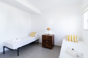 A small, clean room with two single beds, a wooden nightstand with a lamp, and a white wall. - Vilamoura Garden Villa 2 by Homing (Loulé)