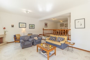 A living room with a fireplace, two sofas, a coffee table, and a staircase leading to another level. - Vilamoura Garden Villa 2 by Homing (Loulé)