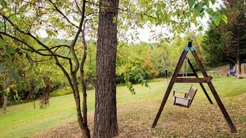 A wooden swing set in a grassy area with trees and a picnic table in the background.