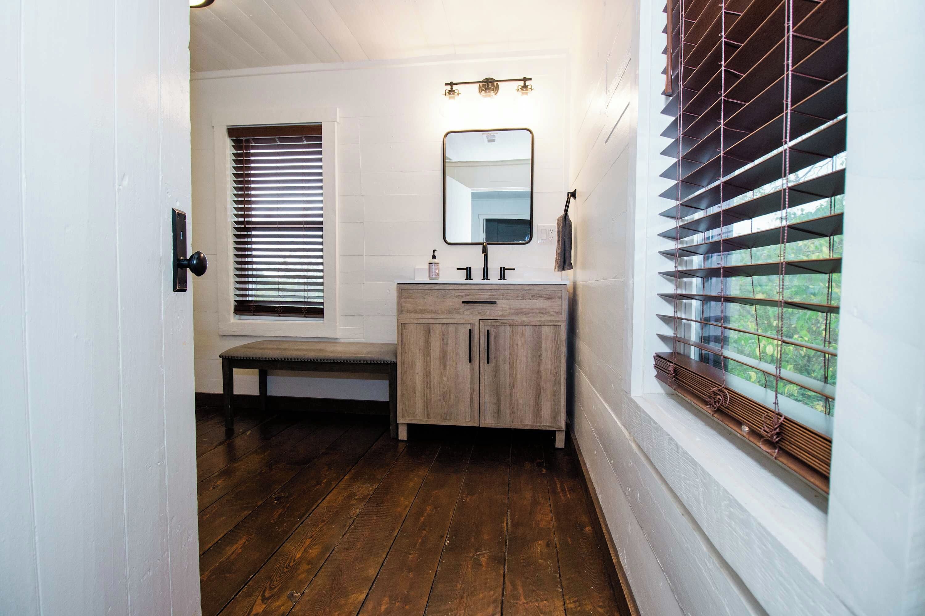 Un bagno con una panca di legno, un lavandino con specchio e una finestra con persiane.