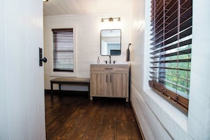 Un bagno con una panca di legno, un lavandino con specchio e una finestra con persiane.