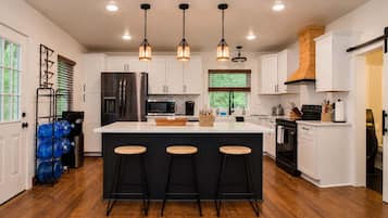 A modern kitchen with white cabinets, a central island with stools, stainless steel appliances, and pendant lighting.