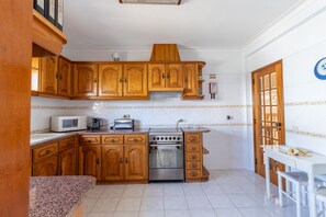 A kitchen with wooden cabinets, a microwave, a toaster, and a stove. - VILAMOURA GARDEN VILLA WITH POOL by HOMING (Vilamoura)