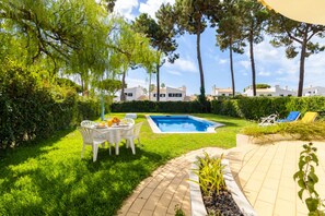 A backyard with a swimming pool, a dining table with chairs, and a lounge area with chairs. - VILAMOURA GARDEN VILLA WITH POOL by HOMING (Vilamoura)