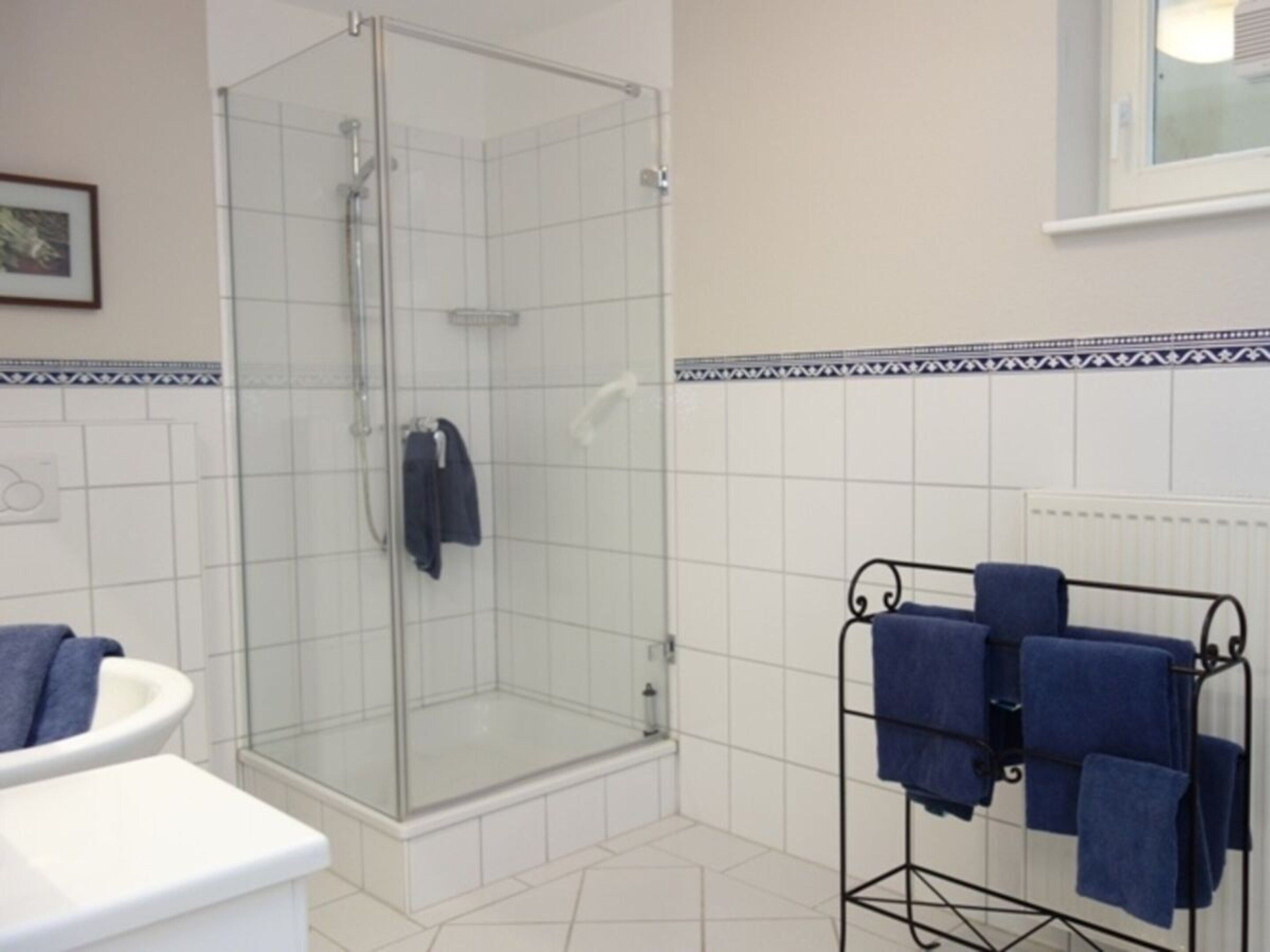 Een badkamer met een douchecabine van glas, een wit toilet en een handdoekrek met meerdere handdoeken.