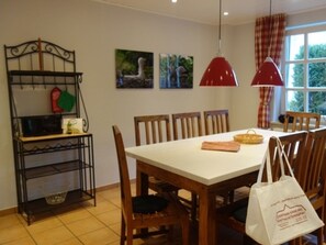 A dining area with a white table, wooden chairs, a red pendant light, and a metal rack with kitchen items. - Holiday Home in Wyk on Fohr With Terrace (Wyk auf Foehr)