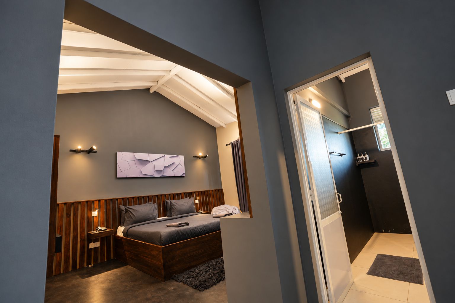 Ein modernes Schlafzimmer mit einem Bett, Nachttischen, einer Wandleuchte und einer Tür zu einem Badezimmer.