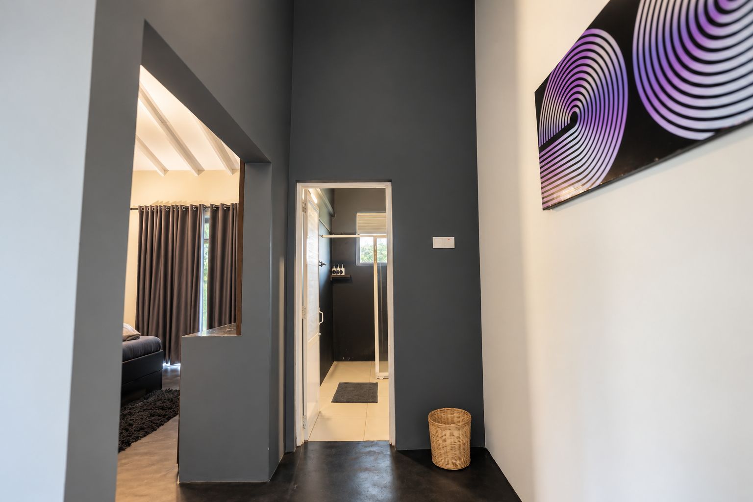 A hallway with a dark wall, a door leading to a bathroom, and a basket on the floor.