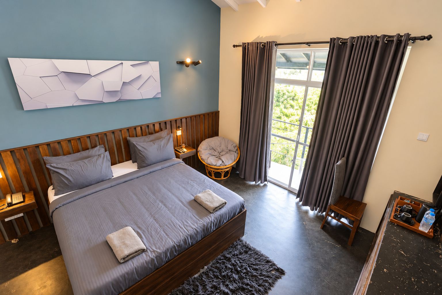 Un dormitorio con una cama grande, una mesita de noche, una lámpara de pared, una silla y una ventana con cortinas.