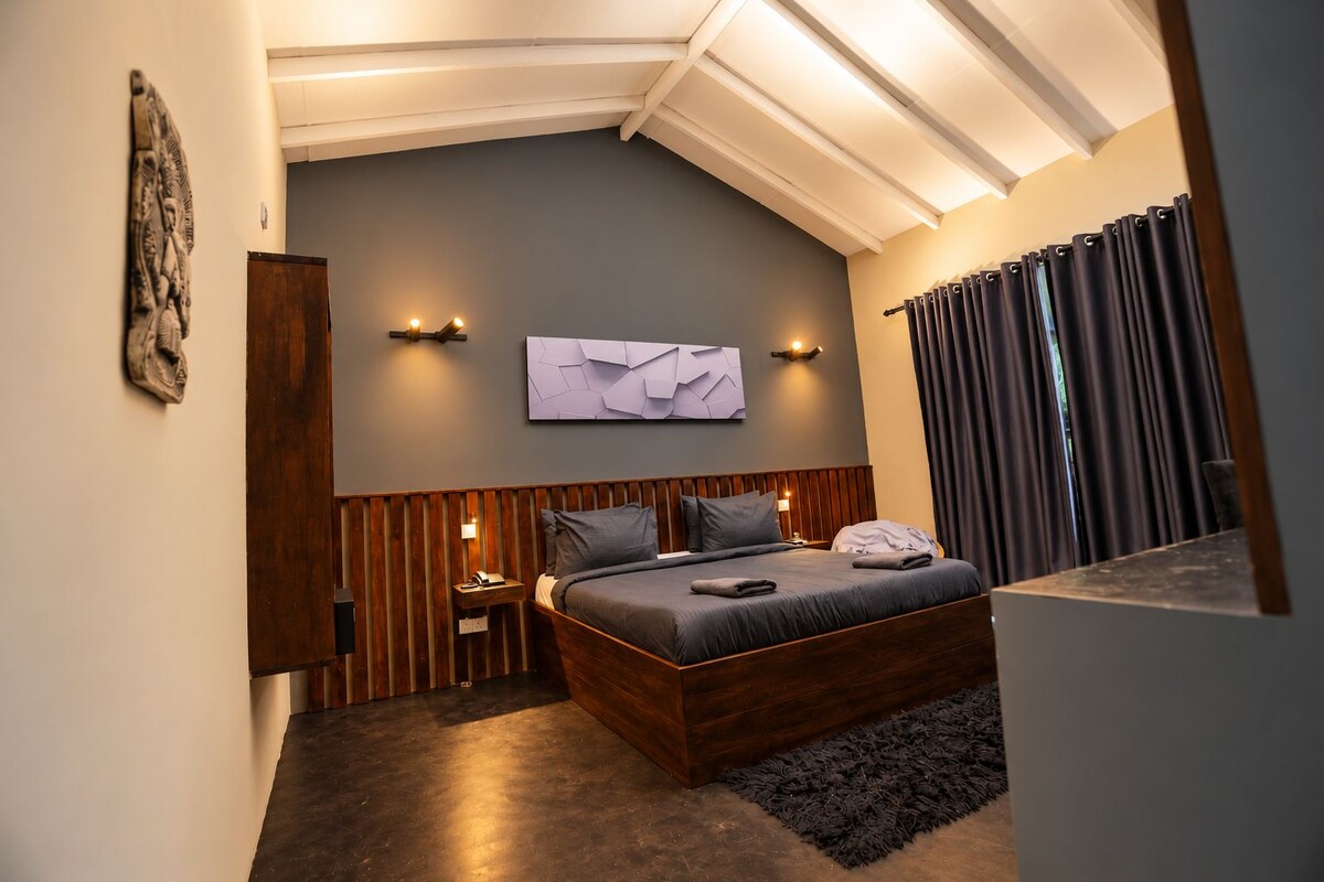 Ein modernes Schlafzimmer mit schrägem Dach, einem Bett mit Holz Kopfteil, einem Nachttisch, einer Wandleuchte und einem großen abstrakten Gemälde.