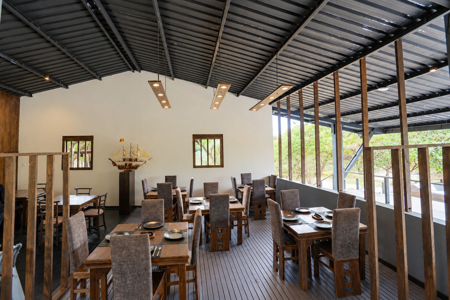 Un espace de restauration intérieur avec des tables et des chaises en bois, de grandes fenêtres et un plafond haut.