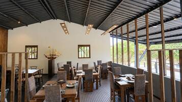 Un espace de restauration intérieur avec des tables et des chaises en bois, de grandes fenêtres et un plafond haut.