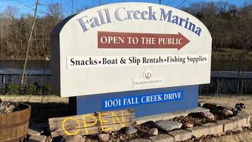 A sign for Fall Creek Marina stating it is open to the public, offering snacks, boat and ship rentals, and fishing supplies.