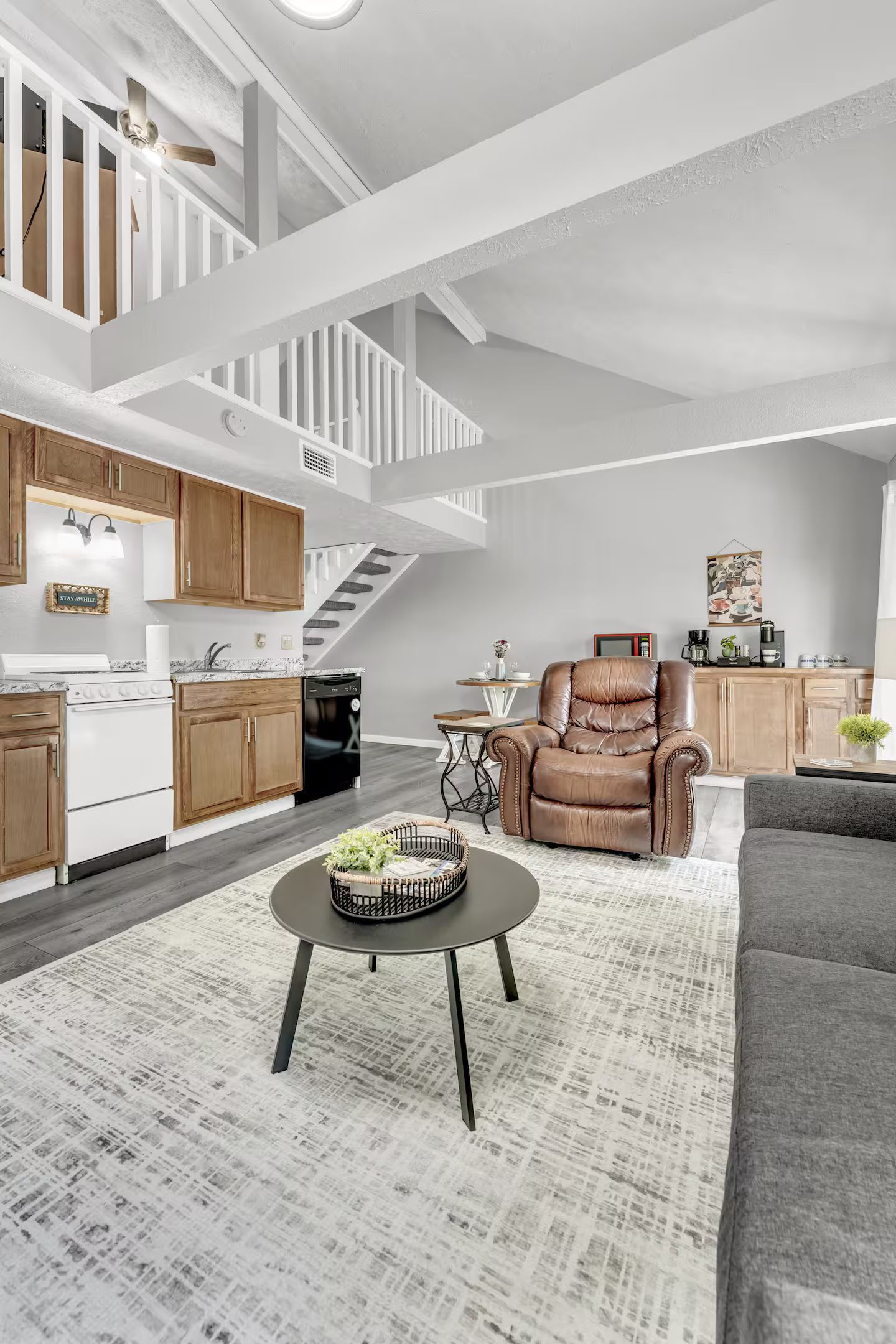 A spacious living area with a staircase, a kitchen, and a seating area with a leather armchair and a sofa.
