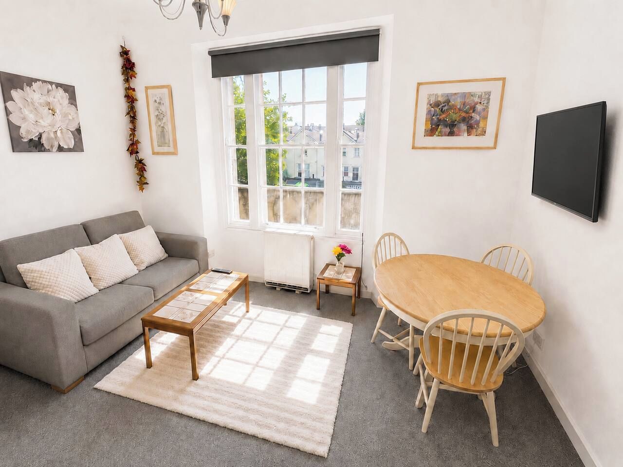 Een woonkamer met een bank, salontafel, eettafel, stoelen en kunstwerken aan de muur.