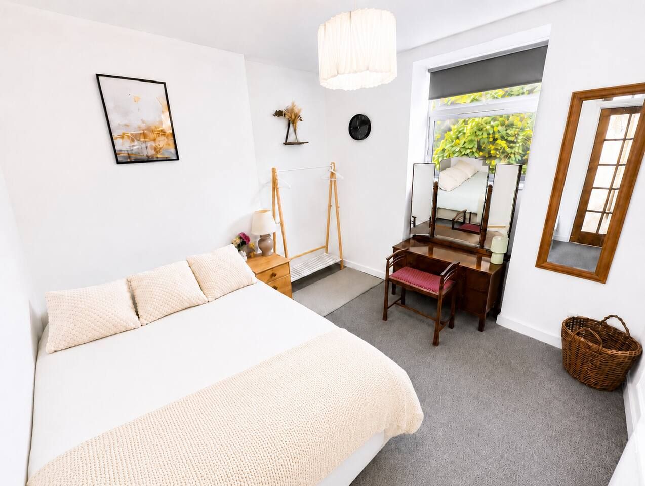 Een slaapkamer met een bed, nachtkastje, lamp en een bureau met stoel. Er is een raam met uitzicht op groen.