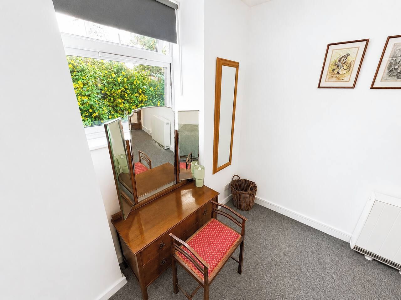 Ein Zimmer mit einem hölzernen Schminktisch, einem roten Sessel, einem großen Spiegel und gerahmten Bildern an der Wand.
