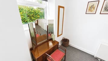 Ein Zimmer mit einem hölzernen Schminktisch, einem roten Sessel, einem großen Spiegel und gerahmten Bildern an der Wand.