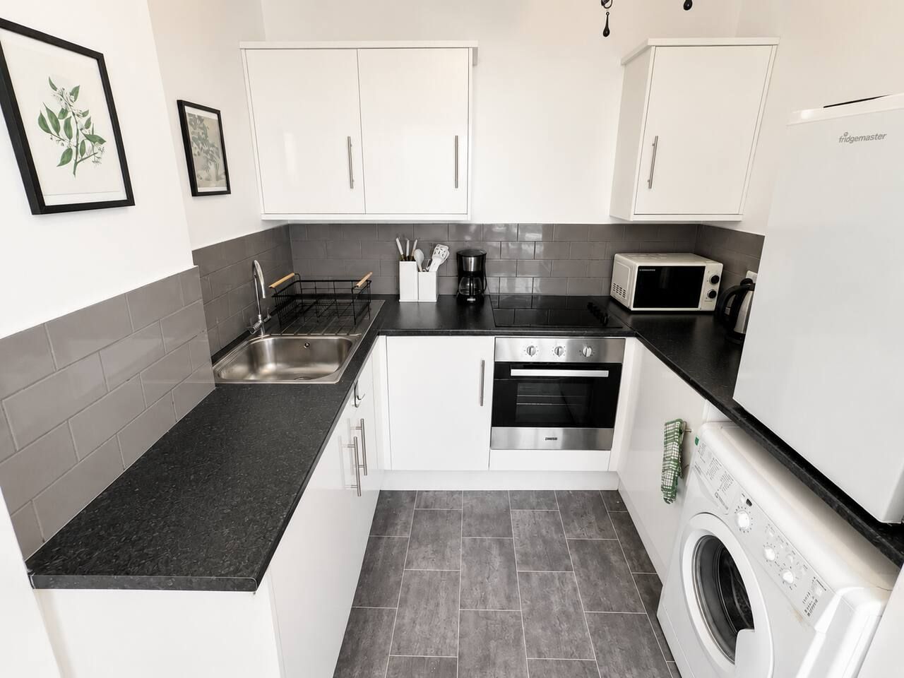 A modern kitchen with white cabinets, a black countertop, a built-in oven, a microwave, and a washing machine.