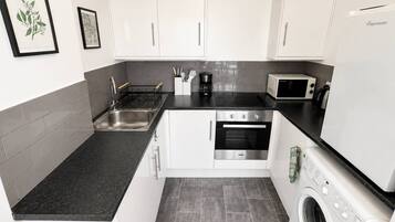 A modern kitchen with white cabinets, a black countertop, a built-in oven, a microwave, and a washing machine.