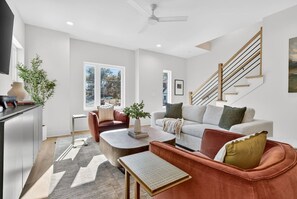 A modern living room with a sofa, armchair, coffee table, and a staircase. - Two Adjacent Homes 8 Bedrooms, Sleeps 20, Rooftop (Nashville)