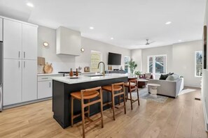 A modern kitchen with a central island, bar stools, and a dining area with a sofa. - Two Adjacent Homes 8 Bedrooms, Sleeps 20, Rooftop (Nashville)