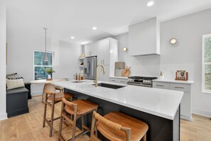 A modern kitchen with a large island, bar stools, stainless steel appliances, and a view of the outdoors. - Two Adjacent Homes 8 Bedrooms, Sleeps 20, Rooftop (Nashville)