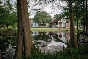 A serene lakeside setting with a wooden dock, a house with a porch, and lush greenery. - Relax & Unwind: Discover the Peaceful Evangeline Suite (Sunset)