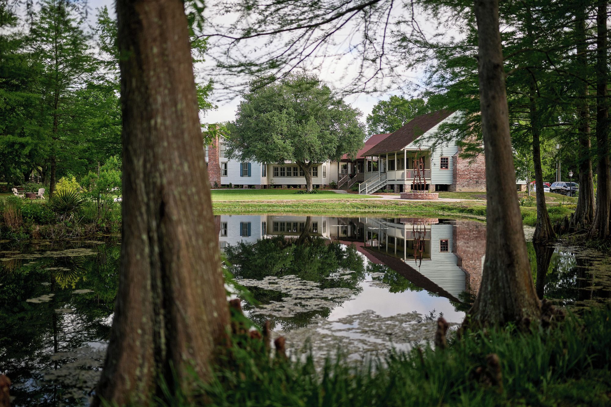 Een vredig meerlandschap met een houten steiger, een huis met veranda, en weelderige begroeiing.