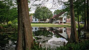 Een vredig meerlandschap met een houten steiger, een huis met veranda, en weelderige begroeiing.