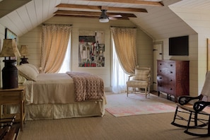 A bedroom with a bed, a dresser, a chair, a rocking chair, a ceiling fan, and a wall-mounted TV. - Family-Friendly Comfort in Acadiana: Fais-Do-Do Suite (Sunset)