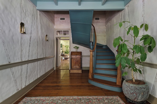 A hallway with a wooden floor, a blue staircase, and a potted plant.