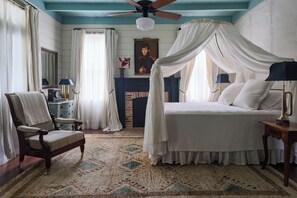 A bedroom with a four-poster bed, a chair, a fireplace, and a ceiling fan. - Garand Suite: Experience Ville Platte’s Heritage in Comfort (Sunset)