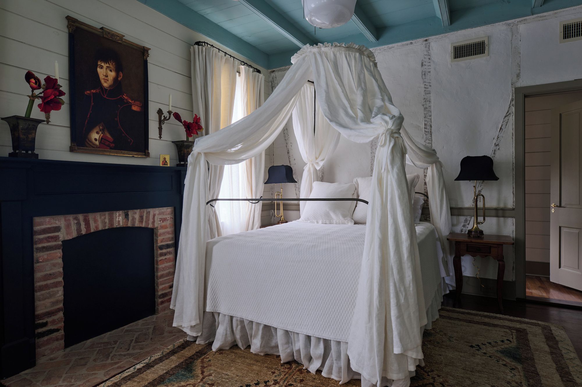 A bedroom with a four-poster canopy bed, a fireplace, and a painting on the wall.