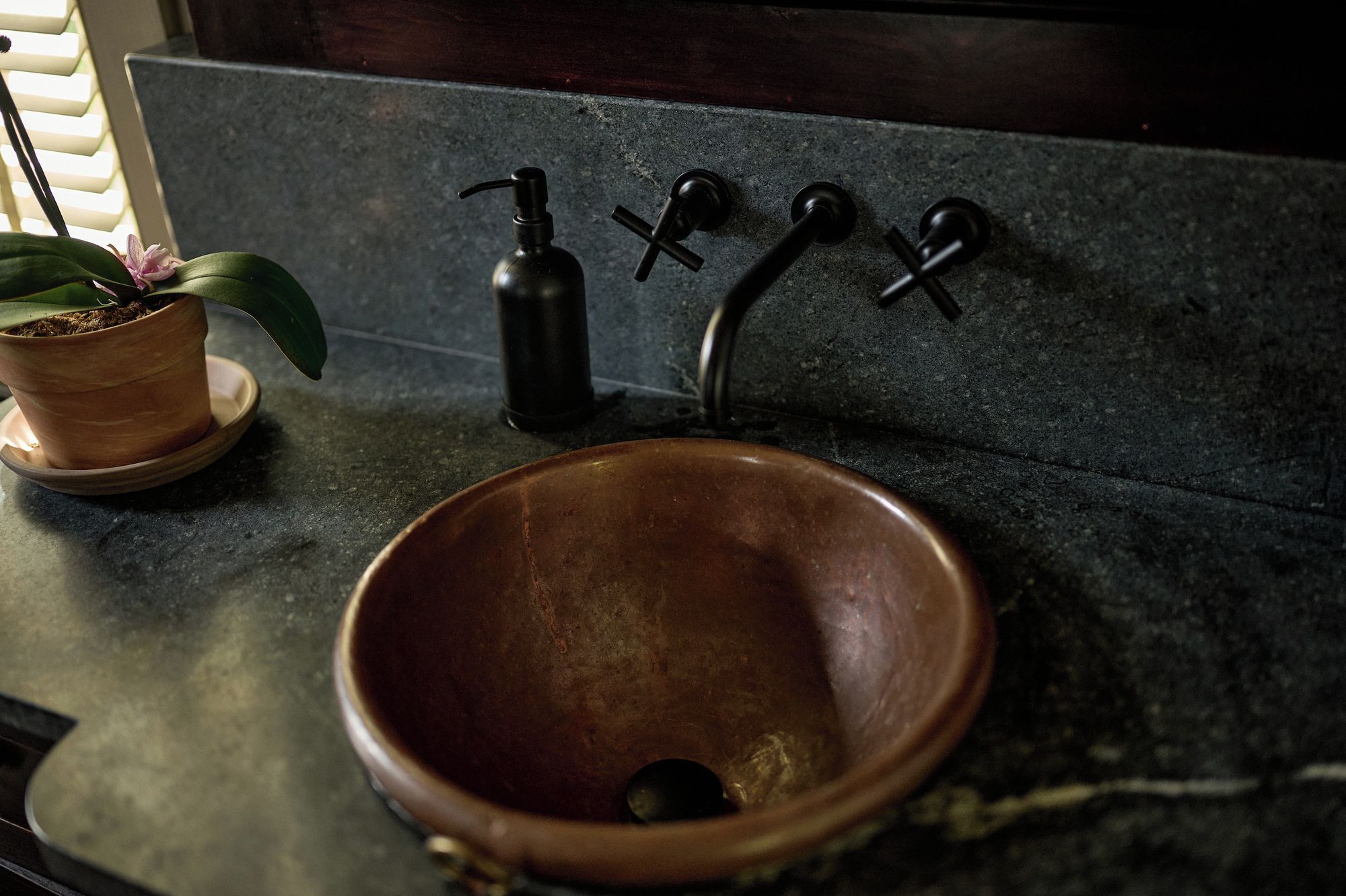 A bathroom with a terracotta sink, a potted plant, and a black faucet.