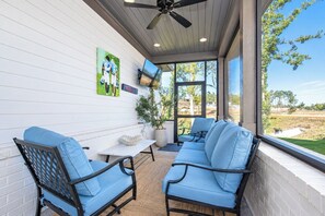 Eine überdachte Terrasse mit zwei blauen Stühlen, einem kleinen Tisch und einem Deckenventilator.