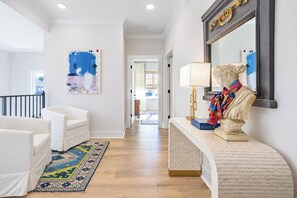 A hallway with a white sofa, a patterned rug, a bust sculpture, and a mirror with a gold frame. - The Pete's Sake, Pool + Grill, 4BR by VDV (Oxford)