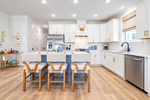 A modern kitchen with white cabinetry, a central island with bar stools, stainless steel appliances, and a dishwasher. - The Pete's Sake, Pool + Grill, 4BR by VDV (Oxford)